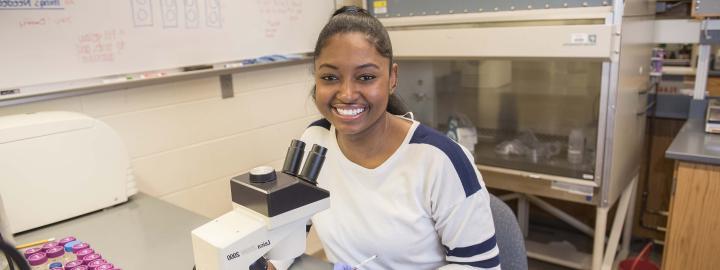 Biology student examining a slide sample on a lab microscope.